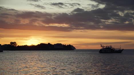 Barco-De-Pescadores-Amarrado-Con-Siluetas-Con-Un-Hermoso-Fondo-Dorado-De-Puesta-De-Sol,-Disco-Solar-Redondo-Frente-A-La-Isla-Tropical-En-El-Paseo-Marítimo-De-Kota-Kinabalu