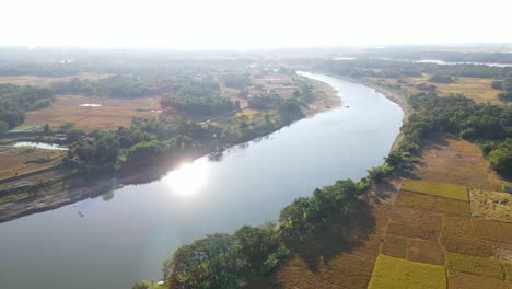 flying-over-Surma-river-surrounded-by-farmland-with-a-village-in-the-distance-in-Sylhet,-Bangladesh-with-beautiful-sunny-weather