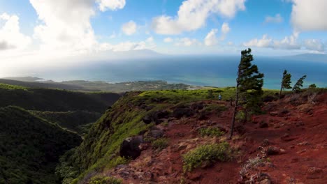 FPV-aerial-view-revealing-two-operators-controlling-the-drone-on-top-of-the-molokai-mountains,-rear-view