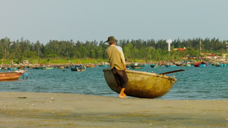 Static-shot-of-a-local-man-dragging-a-small-traditional-boat-from-the-ocean-in-Da-Nang