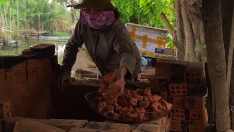 An-Asian-woman-in-a-face-mask-skillfully-removes-freshly-fired-clay-figures-from-a-wood-fired-oven,-showcasing-the-art-and-tradition-of-pottery-making