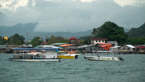 Bay-Area-of-Kampung-Tanjung-Aru-Lama-District,-Travel-Hopping-Tour-Boats-in-Marina-and-Water-Village-Houses-on-Overcast-Sky-Before-Storm-In-Sabah,-Kota-Kinabalu