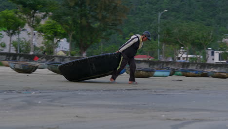 Tracking-shot-of-a-fisherman-dragging-his-boat-to-the-edge-of-the-sea-in-Da-Nang