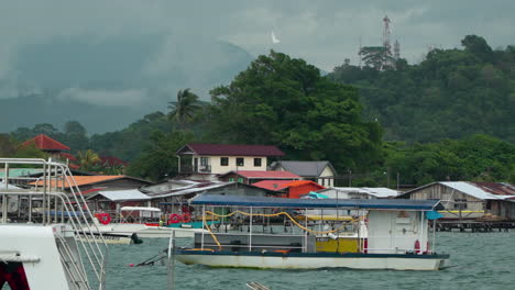 Muchos-Botes-Turísticos-De-Salto-Amarrados-En-La-Costa-De-La-Bahía-De-Kampung-Tanjung-Aru-Lama,-Casas-De-Pueblo-De-Agua-En-El-Fondo-En-Sabah,-Kota-Kinabalu