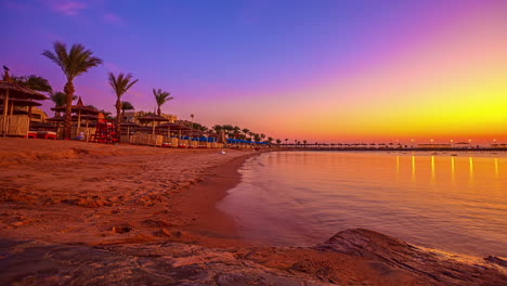 Tiro-De-Lapso-De-Tiempo-De-La-Puesta-De-Sol-Dorada-En-La-Playa-De-Arena-Con-Agua-En-Movimiento-Del-Océano-En-La-Noche---Cielo-Colorido-En-Hurghada,-Egipto