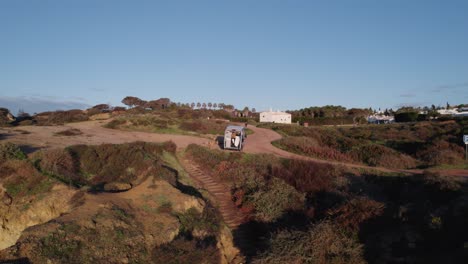 Young-adult-male-drone-operator-sitting-in-motorhome-filming-social-media-selfie-reveal-on-Praia-dos-Arrifes-coastal-beach