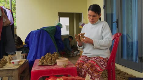 An-Asian-woman-sits-at-a-small-table-crafting-animal-figures-in-clay-for-traditional-Thanh-Ha-flutes,-showcasing-the-beauty-of-cultural-handicrafts