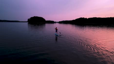 Aerial-of-man-paddle-boarding-on-lake-at-sunset-in-Sweden