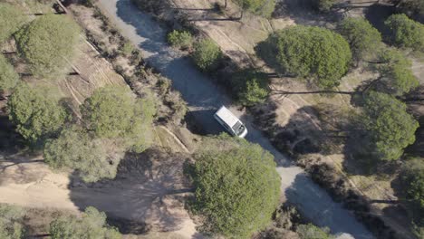 Aerial-view-orbiting-motorhome-driving-through-woodland-wilderness-on-road-trip-in-Spanish-countryside