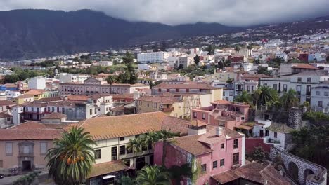 Un-Dron-Sobrevuela-El-Pueblecito-De-Las-Islas-Canarias-En-Tenerife,-Puerto-De-La-Cruz,-Revelando-Una-Casa-En-El-Centro-De-La-Ciudad-Con-Un-Entorno-Tropical-De-Palmeras.
