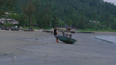 Tracking-shot-of-a-fisherman-dragging-his-boat-away-from-the-ocean-in-Da-Nang