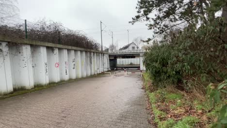 Dunkle-Schmutzige-Bahnunterführung-Für-Fußgänger-Mit-Schiebegitter-Und-Kleinem-Wohnhaus-Im-Hintergrund