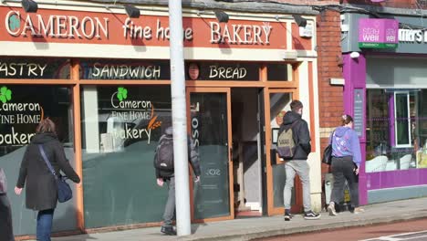 People-walking-Washington-street,-Cork-City,-Ireland,-with-storefronts,-bakery