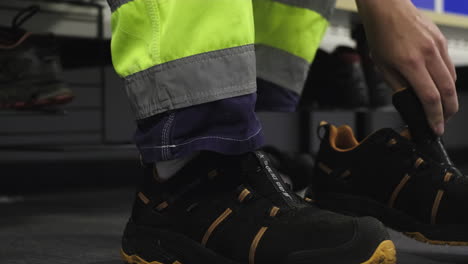 Male-wood-worker-in-a-locker-room-at-a-wood-mass-facility-getting-ready-for-his-shift-as-he-puts-on-work-boots-with-steel-toed-soles-safety-gear-in-hazardous-forestry-industry-locker-room-employee