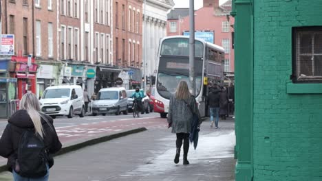 Working-day-on-Washington-street-Cork-City-with-female-pedestrians,-delivery-guy-cycling-and-bus-on-a-bus-station