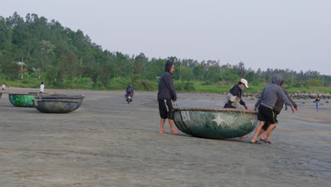Tracking-shot-of-4-men-dragging-a-small-boat-towards-the-water-in-Da-Nang