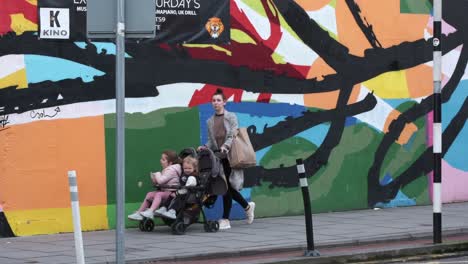 Mujeres-Ocupadas-Con-Dos-Niños-Pequeños-Caminando-Por-La-Calle-Washington,-La-Ciudad-De-Cork,-Irlanda