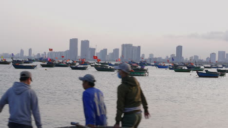 Dolly-shot-with-fishermen-carrying-a-boat-with-Da-Nang-skyline-with-boats-in-the-port