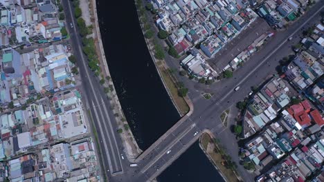 Traffic-bridge-and-overpass-in-Ho-Chi-Minh-City,-Vietnam,-Aerial-view-on-a-sunny-day-featuring-the-canal,-rooftops-and-road-traffic