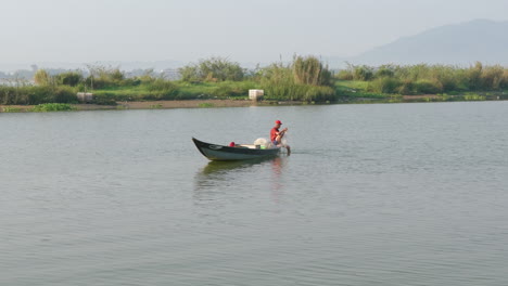 Ruhige-Aufnahme-Eines-Südostasiatischen-Fischers,-Der-Sein-Netz-Justiert,-Während-Er-Auf-Einem-Boot-Mitten-Im-Fluss-Sitzt