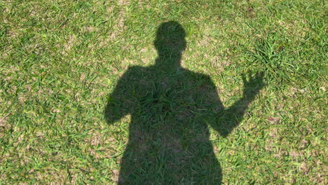 Silhouette-shadow-of-man-standing-in-green-grass-moving-arm-around-on-sunny-day