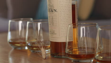 Reihe-Von-Gläsern-Whiskey-Und-Flasche-Auf-Einem-Tisch,-Bereit-Zum-Trinken,-Zeitlupe