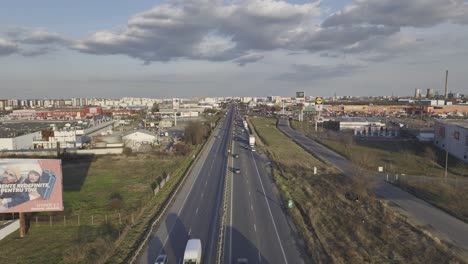 Vuelo-Aéreo-Hacia-Adelante-Sobre-La-Autopista-Con-Automóviles-Y-Camiones-Y-La-Ciudad-De-Bucarest-En-Segundo-Plano