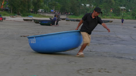 Tracking-shot-of-fishermen-dragging-a-small-traditional-boat-to-the-water-in-Da-Nang