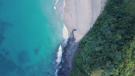 Aerial-tracking-shot-directly-down-on-Nacpan-Beach-on-Palawan,-the-Philippines-from-cliff-at-the-end-with-vegetation-to-Twin-Beach