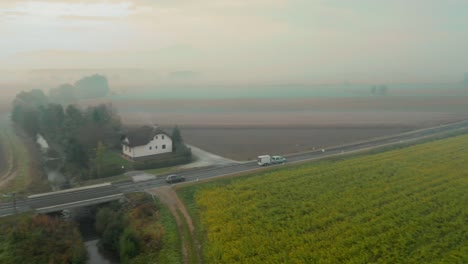 Luftaufnahme-Einer-Straße,-Die-An-Einem-Nebligen-Und-Nebligen-Herbstmorgen-Durch-Ackerland-In-Der-Slowenischen-Landschaft-Führt
