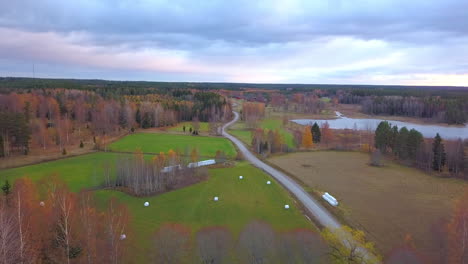 Aerial-drone-shot,-over-the-countryside,-towards-colorful-autumn-trees-and-a-lake,-on-a-cloudy-fall-day,-in-Sweden