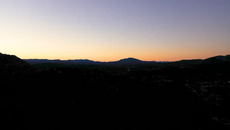 Aerial-view-from-a-mountain-peak-to-reveal-a-town-below-during-sunrise