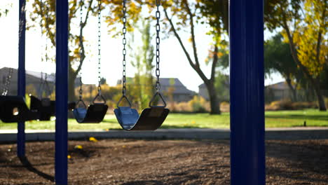 Slide-left-through-a-kids-playground-in-a-park-at-sunrise-with-an-empty-swing-set