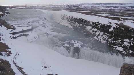 Static,-wide-shot-of-gullfoss-waterfalls-gorge,-on-a-dark,-cloudy-and-snowy,-autumn-day,-on-the-South-coast-of-Iceland
