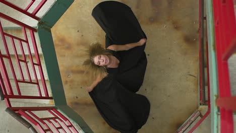 Young-Woman-wearing-a-black-dress-spins-below-a-staircase-at-a-view-from-above