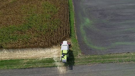 4K-Aerial-slow-motion-shot-of-corn-being-harvested-by-big-combine-harvester-at-noon-on-agricultural-fields-in-Bavaria,-Germany