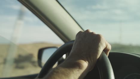 CU-of-man's-hand-on-steering-wheel-in-desert