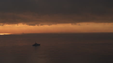 Wide-aerial-view-of-a-Royal-Navy-Warship-sailing-on-a-calm-sea-at-sunrise