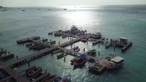 Zwei-Personen-Gehen-Das-Dock-Hinunter-Zu-Den-Booten,-Die-Im-Blauen-Karibischen-Meer-Auf-Aruba-Liegen