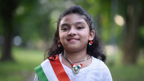 A-cute-little-Indian-girl-is-smiling-and-laughing-at-the-camera-wearing-Indian-tricolor-flag,-closeup,-Slow-motion