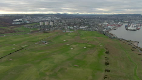 Aerial-view-of-Aberdeen-golf-course-with-the-city-in-the-background-on-a-cloudy-day,-Aberdeenshire,-Scotland