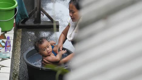 Indonesian-baby-outdoors-next-to-mosaic-tiles-being-bathed-by-her-mother-in-Bali