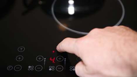 Close-up-of-electric-stove-control-panel,-male-finger-pressing-buttons,-red-LED-indicators-switched-on