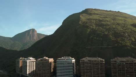 Left-sliding-aerial-view-of-tall-condominium-buildings-with-a-rocky-hill-behind-revealing-in-the-background-the-Corcovado-mountain-with-the-Christ-statue-in-Rio-de-Janeiro,-Brazil