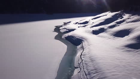 Luftaufnahme-über-Das-Ufer-Eines-Schmelzenden-Zugefrorenen-Sees-Zu-Einem-Riesigen-Bergpanorama-Mit-Großen-Schneebedeckten-Bergen