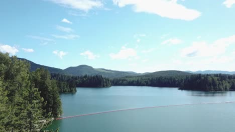 A-vast-aerial-shot-of-a-lake-with-blue-skies-and-forest-filled-shorelines