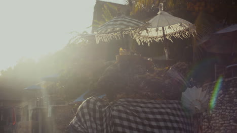 Early-morning-Ceremony-baskets-bathe-in-the-first-light-on-a-beach-in-Uluwatu,-Bali-with-Lens-flare