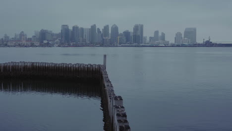 Clip-starts-out-on-wooden-poles-in-water,-then-camera-tilts-up-to-reveal-skyline-of-San-Diego-with-beautiful-reflections-in-the-water