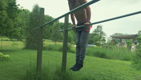 Fit-topless-youth-performs-straddle-front-lever-on-parallel-bars-outdoors-at-home-gym-in-field