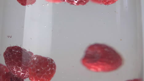 Slow-motion-raspberries-floating-and-splashing-into-glass-of-water-up-close